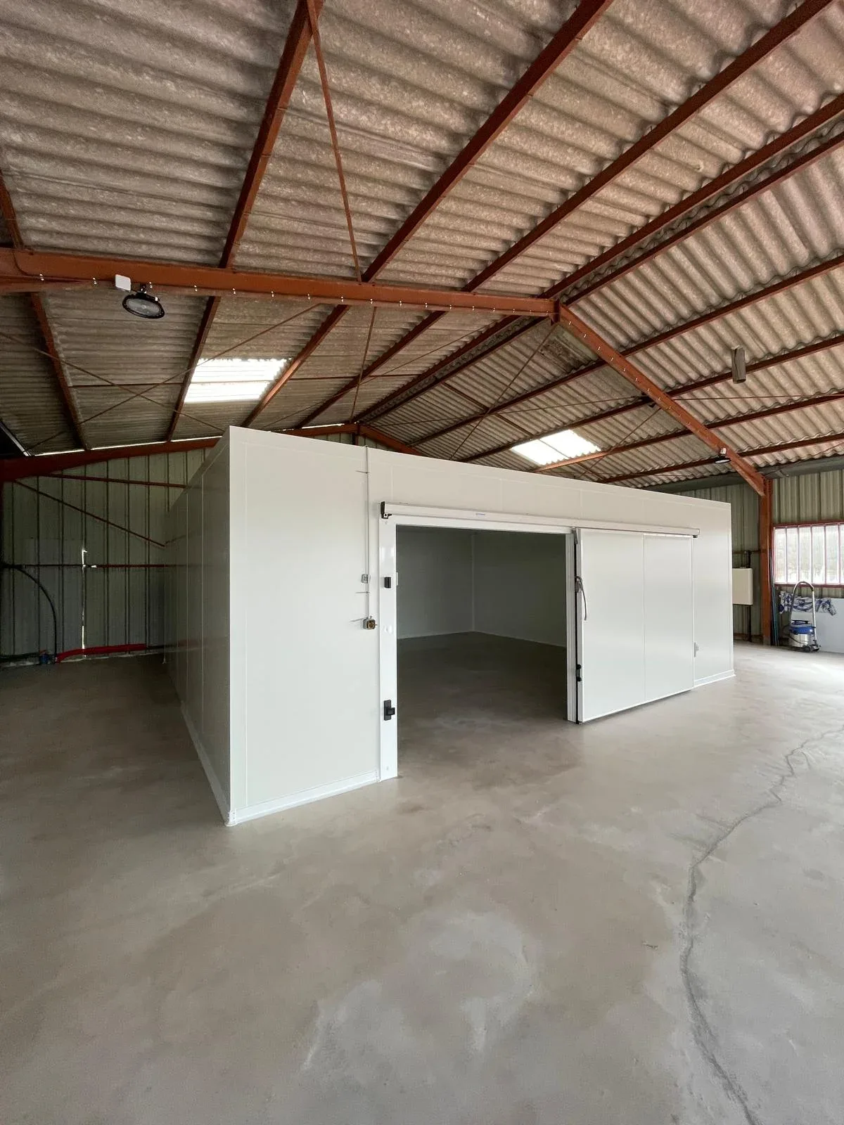 Chambre froide en panneaux isolants avec porte isotherme ouverte dans un hangar
