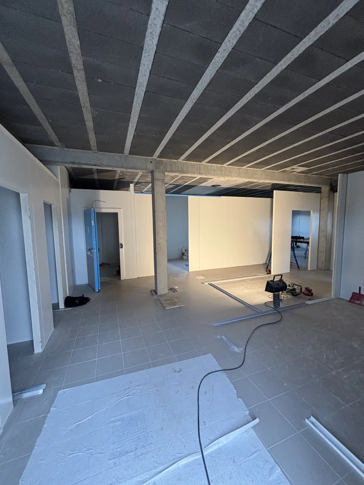 Montage des cloisons en panneaux sandwich PIR d’une cuisine centrale en construction, rails au sol et porte de chambre froide en attente