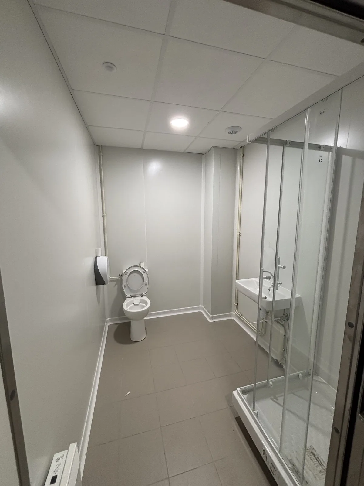 Sanitaires du personnel d’une cuisine centrale en panneaux sandwich blancs avec douche à parois vitrées, WC, lavabo et plafond suspendu